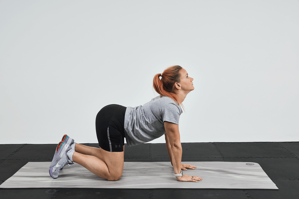 Mujer realizando una postura de yoga en una esterilla, con la espalda arqueada y la cabeza inclinada hacia arriba.